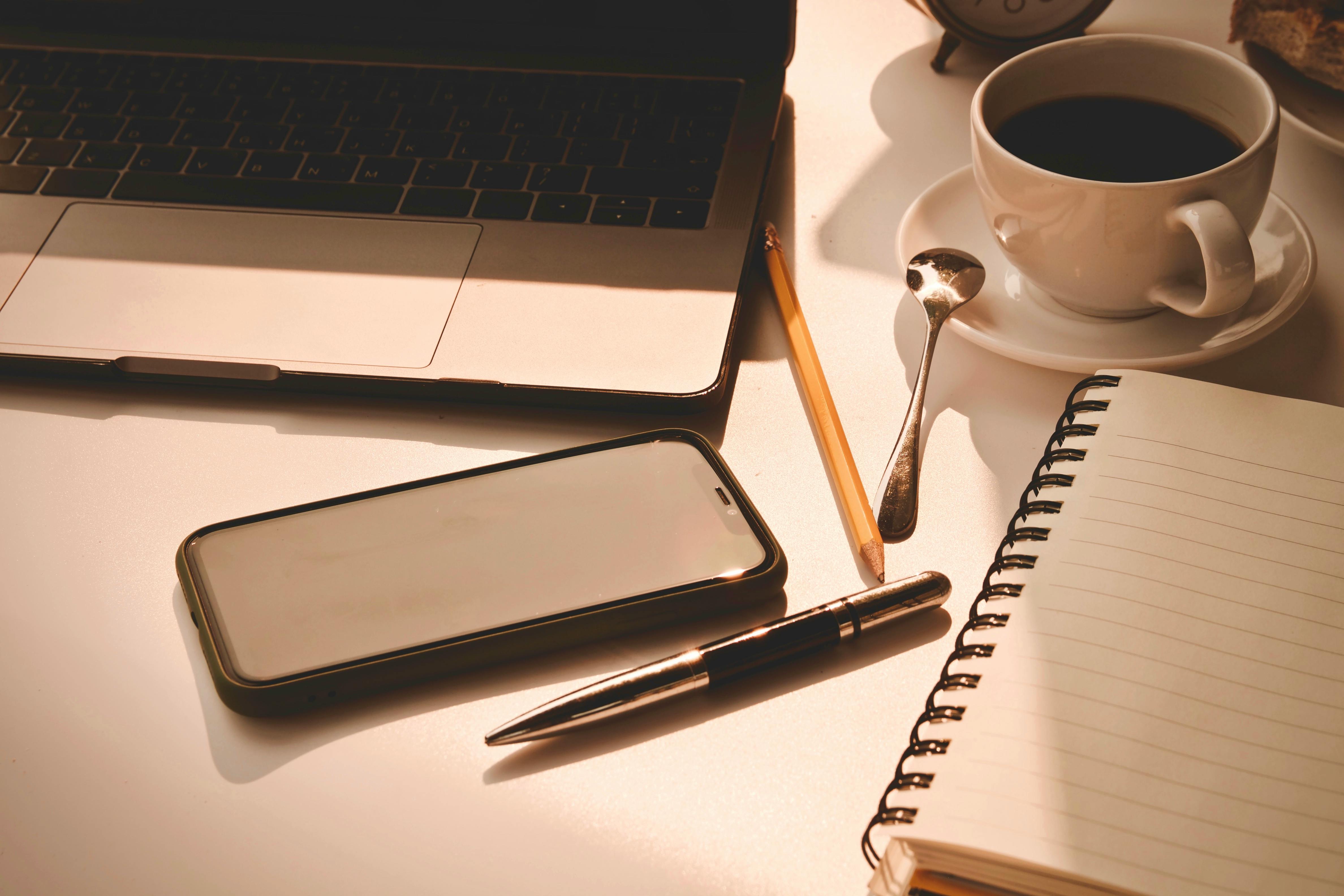 Smartphone resting face down beside a cup and a notebook on a desk