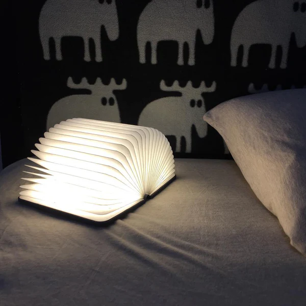 Warm bedside lamp glowing next to an open paperback book in the evening